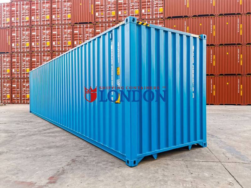 A blue shipping container stands in front of stacked red containers in a storage area.